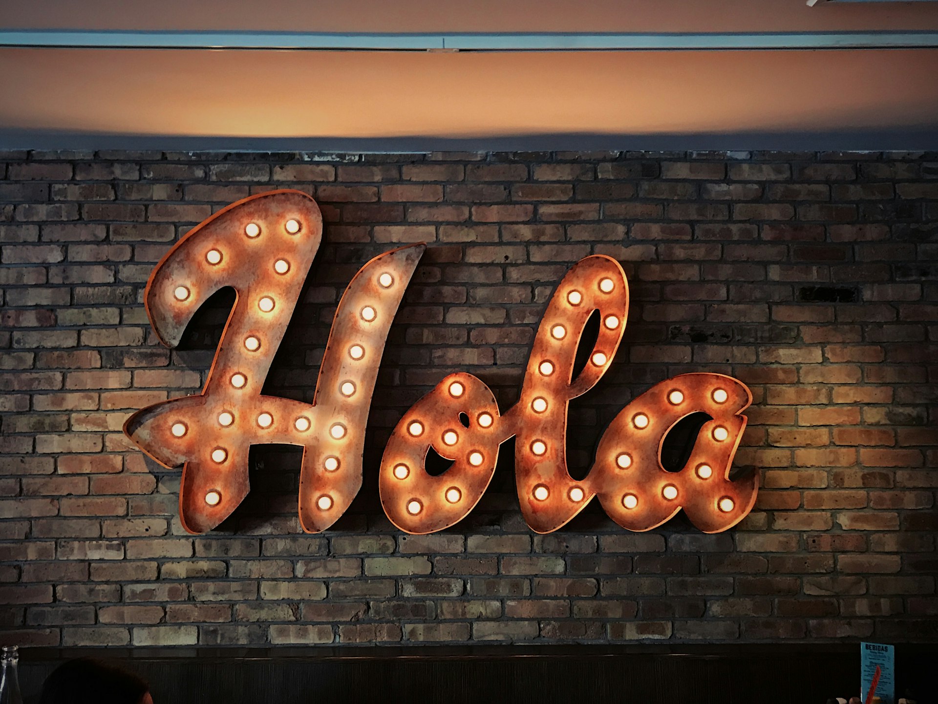 Illuminated 3D letter sign reading 'Hola' mounted on a brick wall, showcasing letter bending craftsmanship.